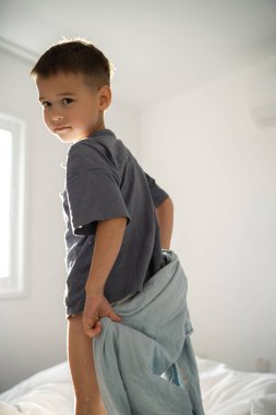 Küçük çocuk elinde parlak bir yatak odasında bir battaniye tutuyor..