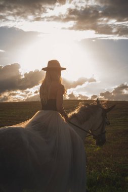Gün batımında beyaz ata binen güzel genç bir kadın.