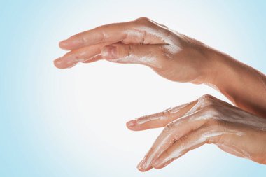 Mavi arka planda nemlendirici losyon kullanan eller