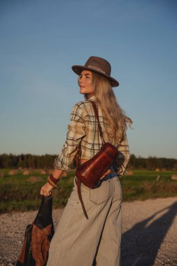 Şık bir kadın kırsal alanda çakıllı bir yolda yürüyor..