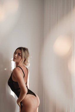 Saf Siyah İç Çamaşırlı Zarif Kadın Beyaz Duvara Karşı Sıcak Bokeh Işığında Poz Veriyor.