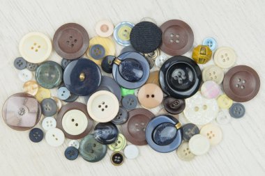 Variety of buttons of different colors and sizes on a light wooden background. Top view.