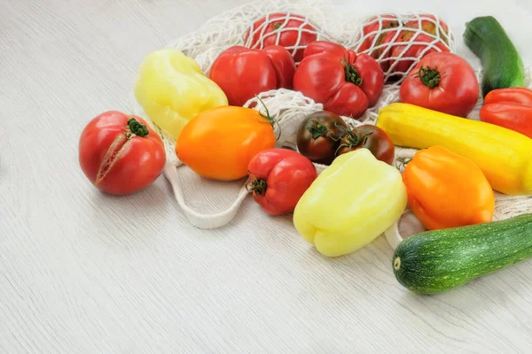 Tomatoes and peppers on a white wooden background. Various farming vegetable in cotton bag. Top view. Copy space.