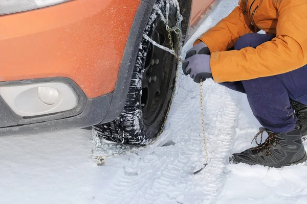 Vehicle equipment for off-road and bad weather. Driver installs chains on the wheel of his car in winter.