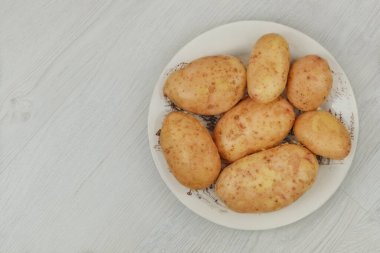 Ahşap arka planda seramik tabakta patates. Hasat ve organik bahçe işleri. Köy hayatı. Yemek yapmak. Üst görünüm.
