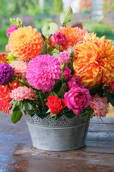 Güller, asterler, elma bahçesindeki ahşap bir masada dahilia. Çiçeksel tasarım. Güneşli bir günde çiçekler. Köy hayatı. Dikey görünüm.