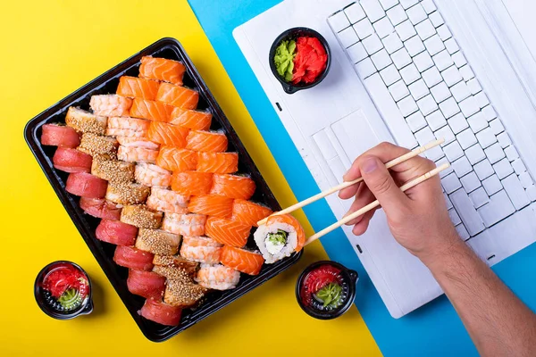 set of rolls, sushi and laptop in the office blue and yellow background. Japanese lunch at the workplace. salmon and wasabi soy sauc