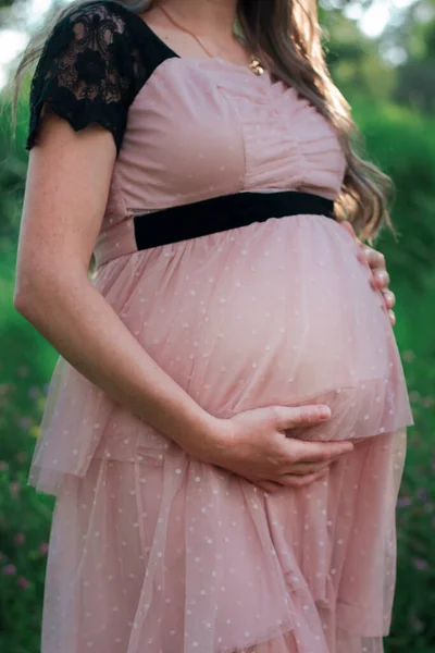 Pregnant belly. A woman shows her pregnant belly. Cute pink dress. Nature