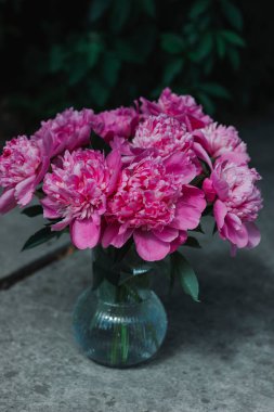 Yeşil bulanık bir bahçe arka planında, cam vazoda pembe şakayıklar.