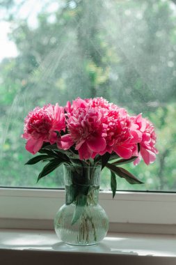 Yeşil bulanık bir bahçe arka planında, cam vazoda pembe şakayıklar.