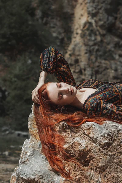 stock image Strong-willed free strong red-haired woman in an ethnic dress near a big stone. A symbol of indomitability. Career