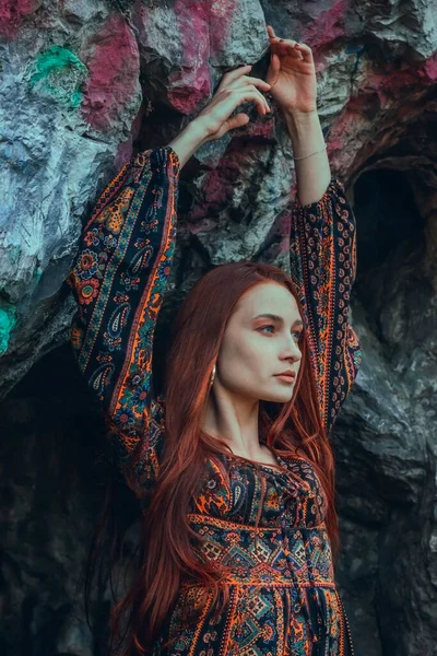 Güçlü iradeli, güçlü kızıl saçlı bir kadının portresi. Büyük bir taşın yanında etnik bir elbise giymiş. Yenilmezliğin sembolü. Kariyer. Moda fotoğrafı. Kavram