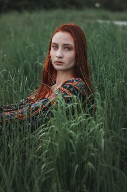 Etnik elbise giymiş kızıl saçlı bir kızın portresi. Yeşil çimenler. Dağ. Doğayla birleşiyor. Kavram