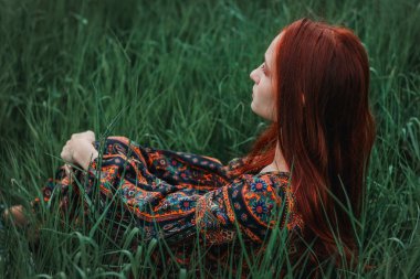 Etnik elbise giymiş kızıl saçlı bir kızın portresi. Yeşil çimenler. Dağ. Doğayla birleşiyor. Kavram