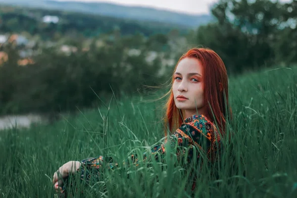 Etnik elbise giymiş kızıl saçlı bir kızın portresi. Yeşil çimenler. Dağ. Doğayla birleşiyor. Kavram