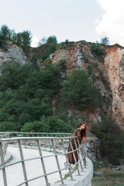 Kariyer geçmişi olan, etnik giysili, uzun boylu, kendine güvenen kızıl saçlı bir kız. Kocaman taşlar. Kızıl saçlar rüzgârda gelişir. Kavram. İradenin ve boyun eğmezliğin sembolü.