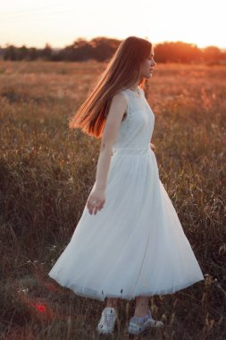 Güzel bir kız gün batımında beyaz bir elbiseyle bir tarlada dans ediyor. Mutlu kadın. Kavram. Gelin