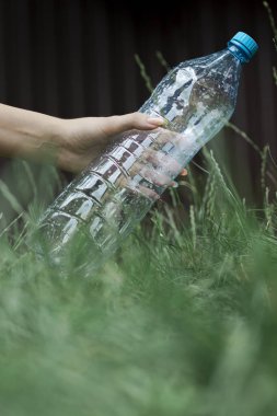 Ekoloji konsepti. İnsan çimenlere plastik bir şişe atar.