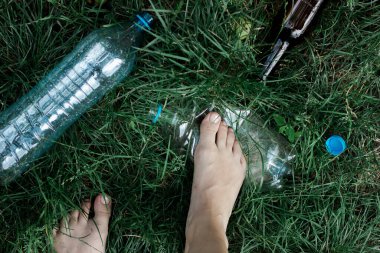 Ekoloji konsepti. Bir insan çimenlere atılan plastik şişeleri ezer.