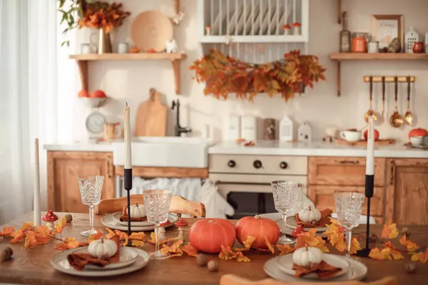 Autumn kitchen interior. Red and yellow leaves and pumpkins on a light background. Serving the dinner table