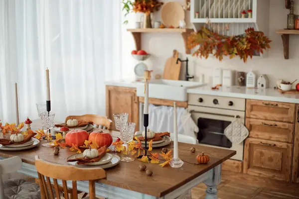 Autumn kitchen interior. Red and yellow leaves and pumpkins on a light background. Serving the dinner table