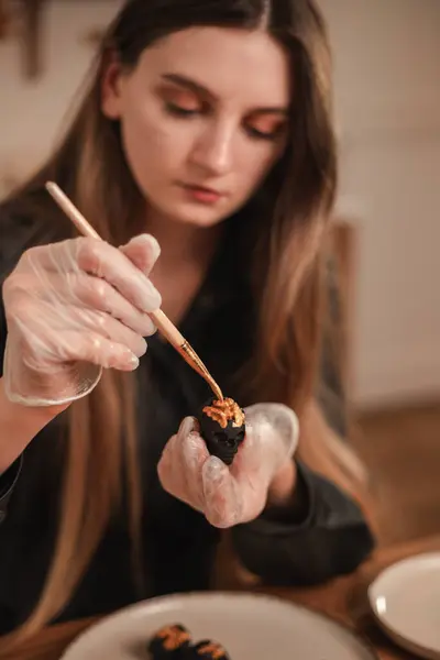 Woman confectioner decorates candy in the form of black skulls for Halloween with gold. The process of creating candies for Halloween