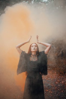 Gotik kadın, sonbahar ormanında kızıl saçlı cadı, siyah elbiseli sis, Cadılar Bayramı. Mistik atmosfer