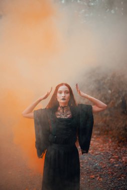 Gotik kadın, sonbahar ormanında kızıl saçlı cadı, siyah elbiseli sis, Cadılar Bayramı. Mistik atmosfer