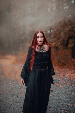 Gotik kadın, sonbahar ormanında kızıl saçlı cadı, siyah elbiseli sis, Cadılar Bayramı. Mistik atmosfer