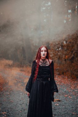 Gotik kadın, sonbahar ormanında kızıl saçlı cadı, siyah elbiseli sis, Cadılar Bayramı. Mistik atmosfer