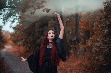 Gotik kadın, sonbahar ormanında kızıl saçlı cadı, siyah elbiseli sis, Cadılar Bayramı. Mistik atmosfer