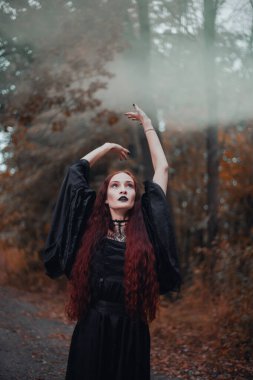 Gotik kadın, sonbahar ormanında kızıl saçlı cadı, siyah elbiseli sis, Cadılar Bayramı. Mistik atmosfer