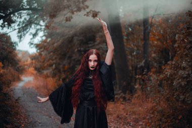 Gotik kadın, sonbahar ormanında kızıl saçlı cadı, siyah elbiseli sis, Cadılar Bayramı. Mistik atmosfer