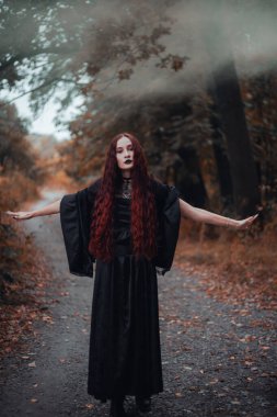 Gotik kadın, sonbahar ormanında kızıl saçlı cadı, siyah elbiseli sis, Cadılar Bayramı. Mistik atmosfer