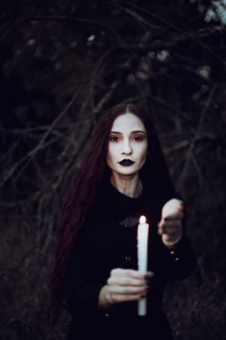 Siyah kostümlü cadı karanlık bir ormanda mum tutuyor. Gizemli atmosfer, ayin, cadılar bayramı.
