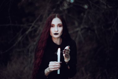Siyah kostümlü cadı karanlık bir ormanda mum tutuyor. Gizemli atmosfer, ayin, cadılar bayramı.