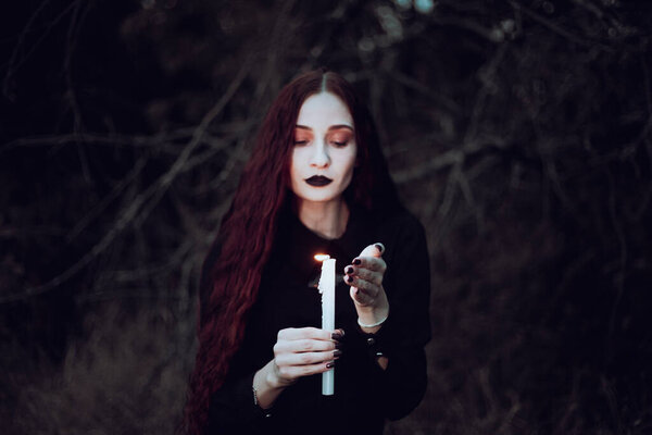 Ведьма в черном костюме держит свечу в темном лесу, таинственная атмосфера, ритуал, Хэллоуин