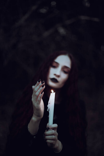 Ведьма в черном костюме держит свечу в темном лесу, таинственная атмосфера, ритуал, Хэллоуин