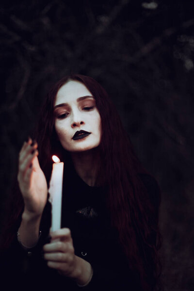 Ведьма в черном костюме держит свечу в темном лесу, таинственная атмосфера, ритуал, Хэллоуин