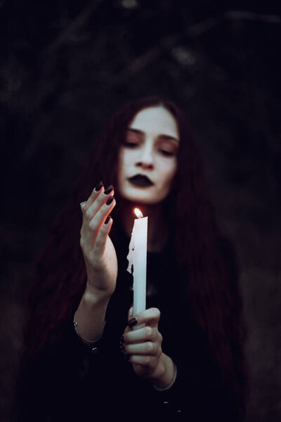 Ведьма в черном костюме держит свечу в темном лесу, таинственная атмосфера, ритуал, Хэллоуин