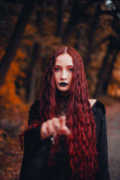 Mysterious gothic girl in dark witch clothes on autumn forest background, halloween