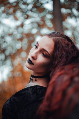 Büyüleyici kızıl saçlı cadı sonbahar ormanında büyülü bir atmosferi var, Cadılar Bayramı.