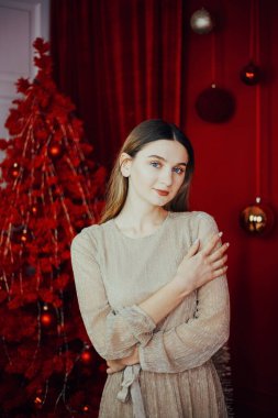 Zarafet ve şenlik ruhu kırmızı temalı bir ortamda süslenmiş bir Noel ağacının yanında duran bir kadınla.