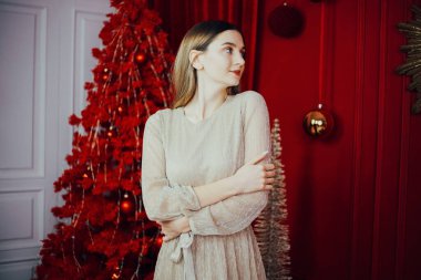 Zarafet ve şenlik ruhu kırmızı temalı bir ortamda süslenmiş bir Noel ağacının yanında duran bir kadınla.