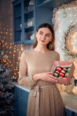 Neşeli bir şekerci güzel dekore edilmiş bir yerde bir kutu renkli badem kurabiyesi sergiliyor. Ağaç ve peri ışıklarıyla yeni yıl kutlamaları için mükemmel..