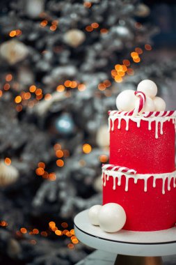 Süslü bir Noel ağacının arka planında iki katlı kırmızı pasta, pasta süsleme fikri, Noel atmosferi, bokeh