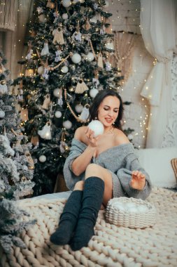 Woman in cozy sweater decorates holiday tree with ornaments during Christmas season in a festive indoor setting clipart