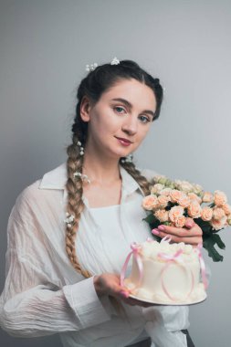 Saçları örgülü pastayla gülümseyen bir şekerci ve ellerinde bir buket çiçek, neşeli bir ruh.