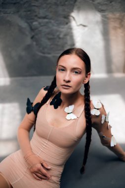 Bir modelin portresi, yumuşak doğal ışık sırasında sakin bir iç mekanda kelebeklerle zarifçe oturuyor.