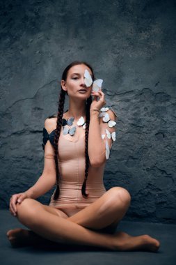 Kadın, gündüz vakti açık havada bir duvarda kelebekler dolaşırken bir kelebeği yüzüne yakın tutuyor.